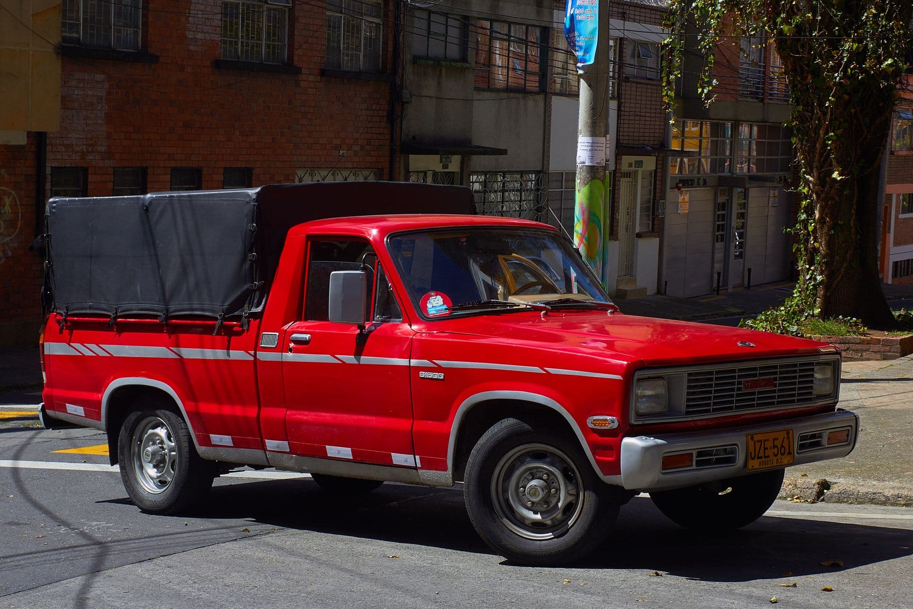 Camioneta roja de modelo antiguo estacionada junto al andén en una calle residencial de Bogotá