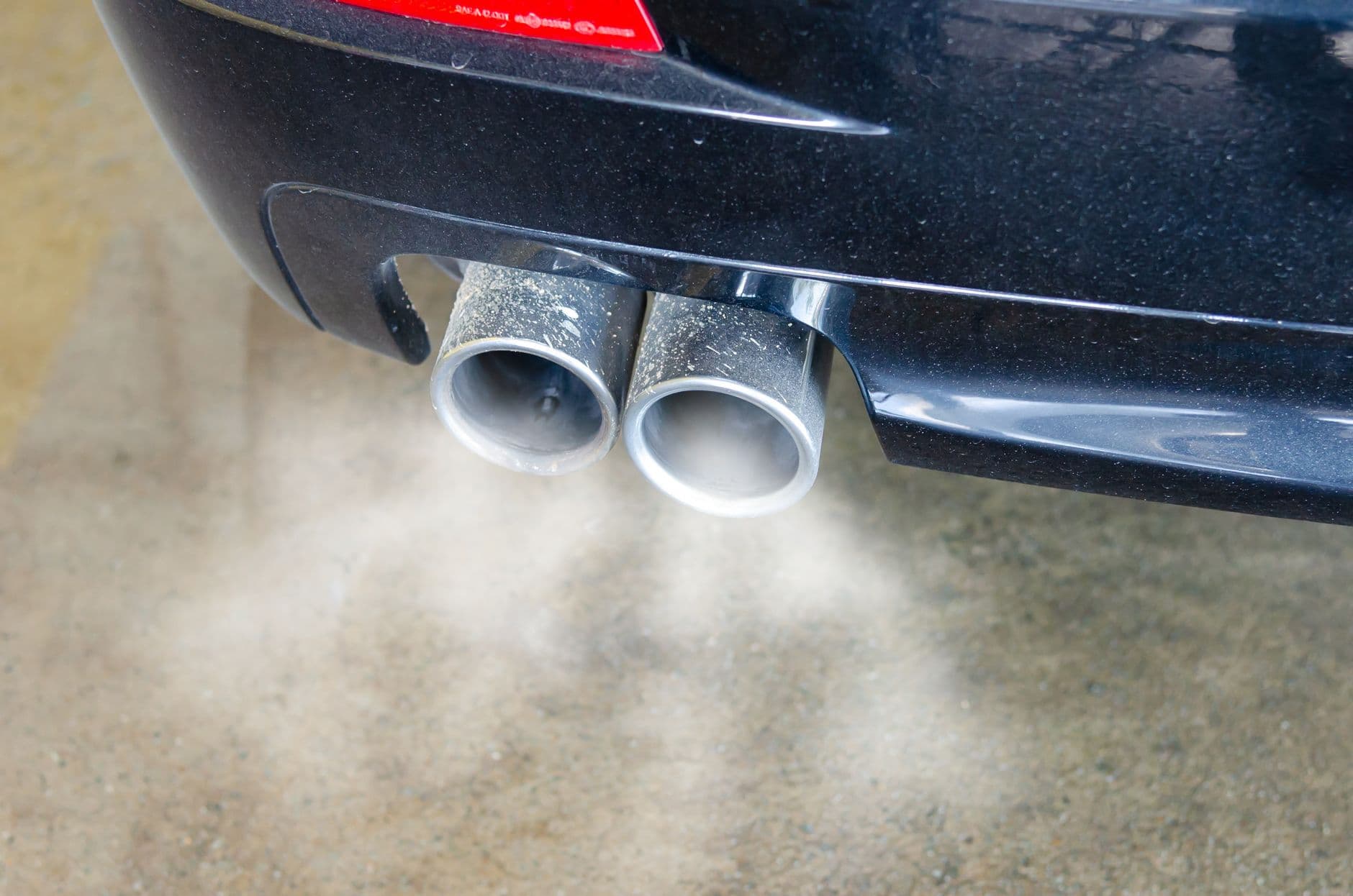 Primer plano de los dos exhostos de un carro oscuro echando humo blanco sobre el pavimento
