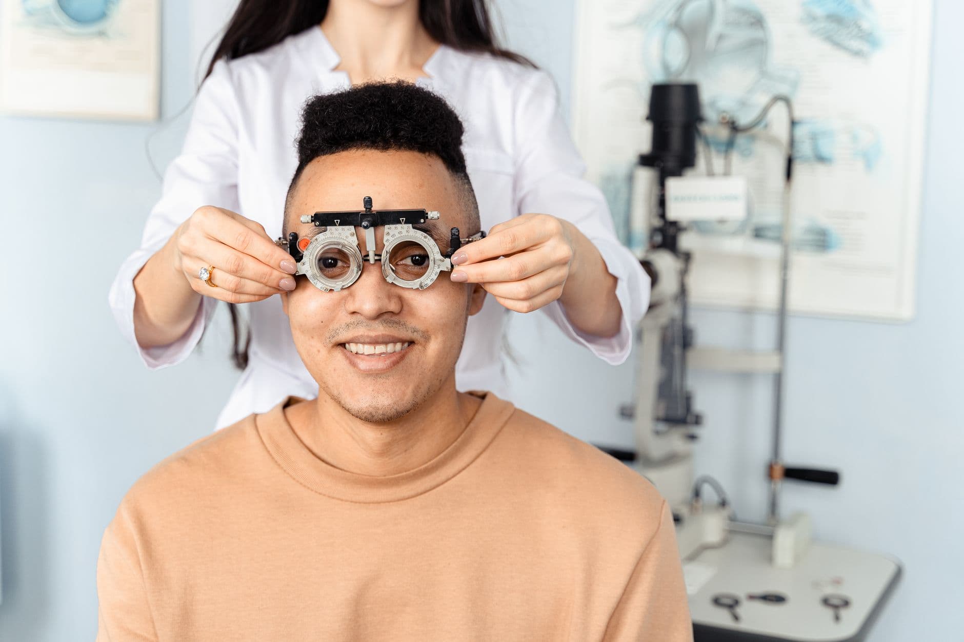 Una optometrista sostiene una montura de pruebas sobre los ojos de un hombre sentado en el consultorio