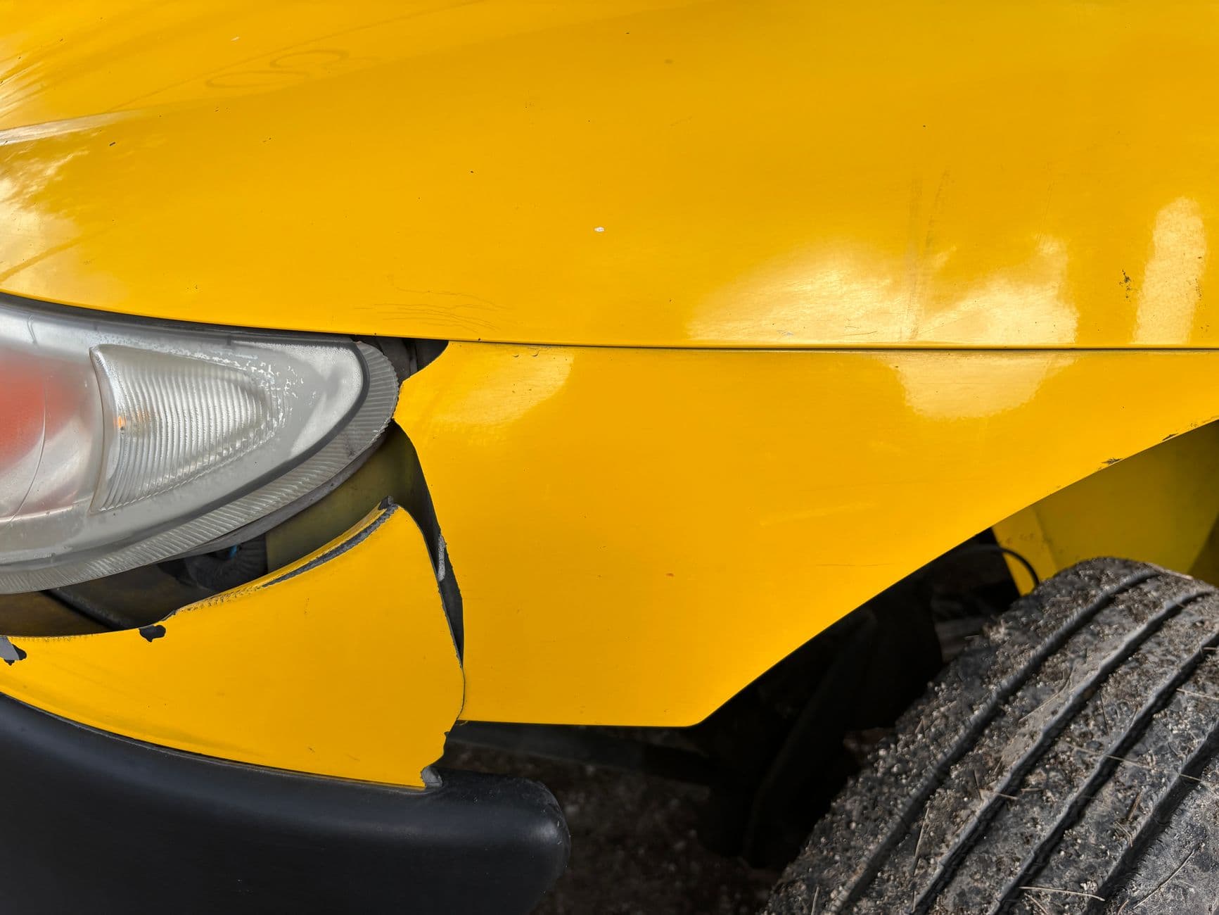 Primer plano del bómper delantero de un carro amarillo abollado y roto