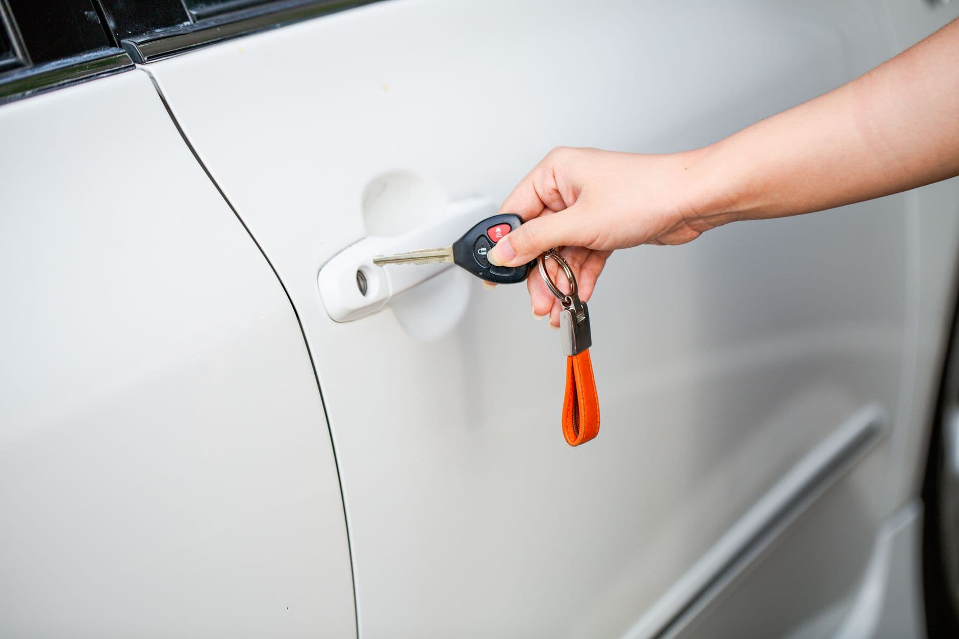 Una mano introduce la llave con control remoto en la cerradura de la puerta de un carro blanco