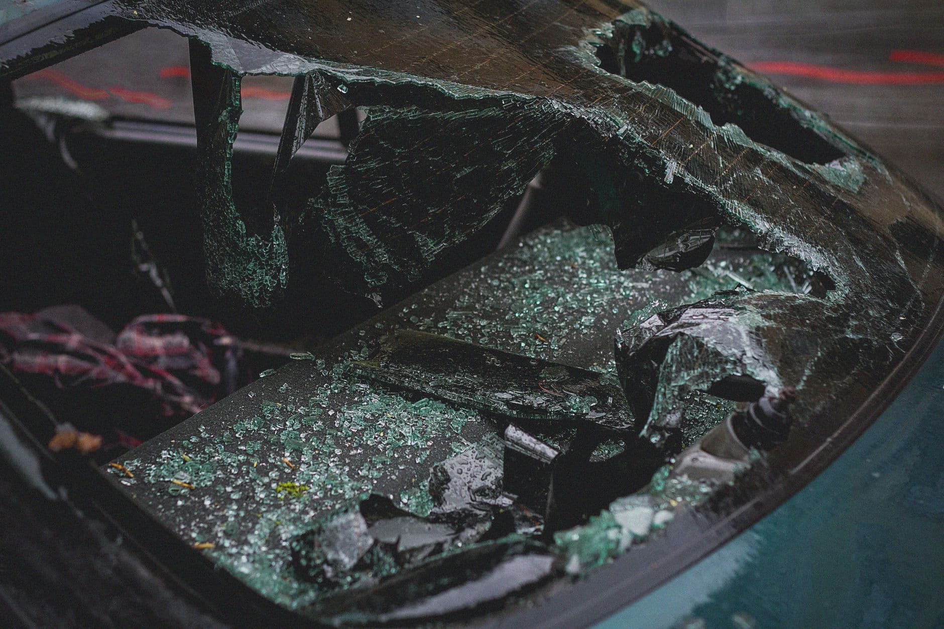 Primer plano del parabrisas de un carro reventado, con el vidrio hecho añicos sobre el tablero