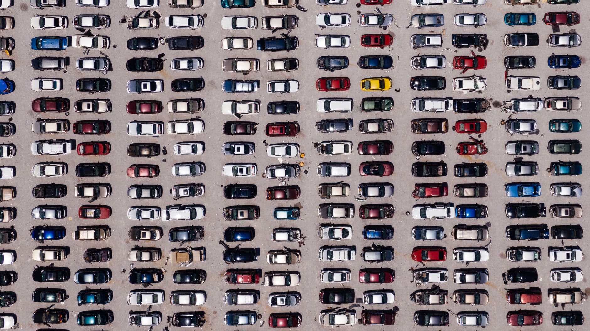 Vista cenital de un patio de vehículos con cientos de carros estacionados en filas apretadas sobre el asfalto
