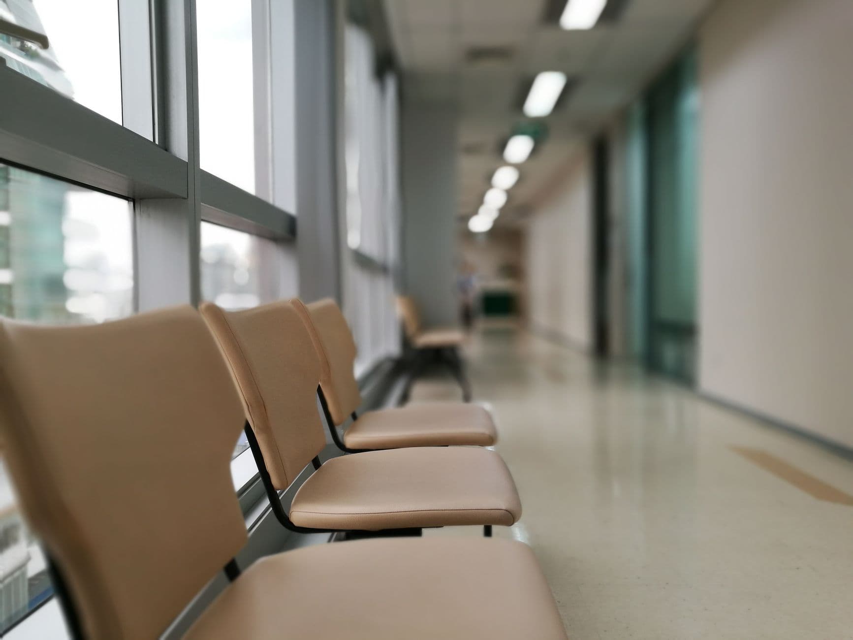 Sillas vacías en el pasillo de espera de un hospital, con la luz entrando por el ventanal