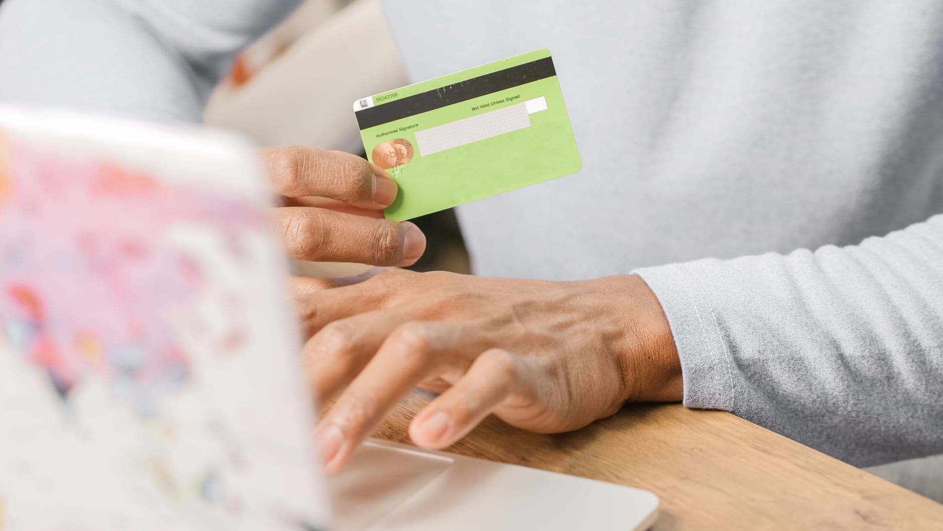 Primer plano de unas manos sosteniendo una tarjeta bancaria verde frente a un computador portátil, en el momento de pagar en línea